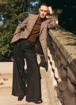 A.P.C. x Anastasia Barbieri campaign image, featuring a female model wearing a blazer, brown sweater, dark pants, on a stair case.