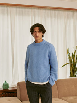 A.P.C. The Brand - man wearing blue sweater and pinstriped pants standing in front of a couch.