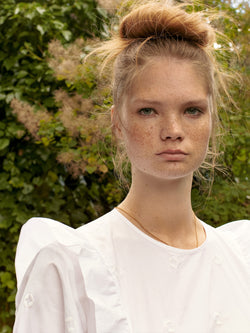 A.P.C. The Brand - woman wearing whit blouse standing in front of trees.