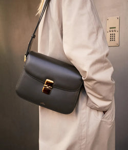 A.P.C. Fall/Winter Campaign - Woman standing by a door wearing an ecru coat and black crossbody bag on shoulder.