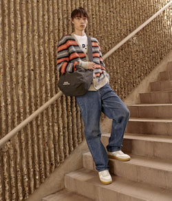 A.P.C. Fall/Winter Campaign - Man on stairs leaning against wall wearing multicolored cardigan and blue jeans.